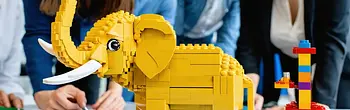 Das Bild zeigt eine Lego-Landschaft auf einem Tisch. Die Komposition umfasst Inseln, Wasserflächen und verschiedene Bauwerke aus Lego. Die Szenerie wirkt spielerisch und kreativ, möglicherweise als Ergebnis eines Workshops oder einer Teambuilding-Übung. Die Details deuten auf eine freie und fantasievolle Gestaltung hin.
